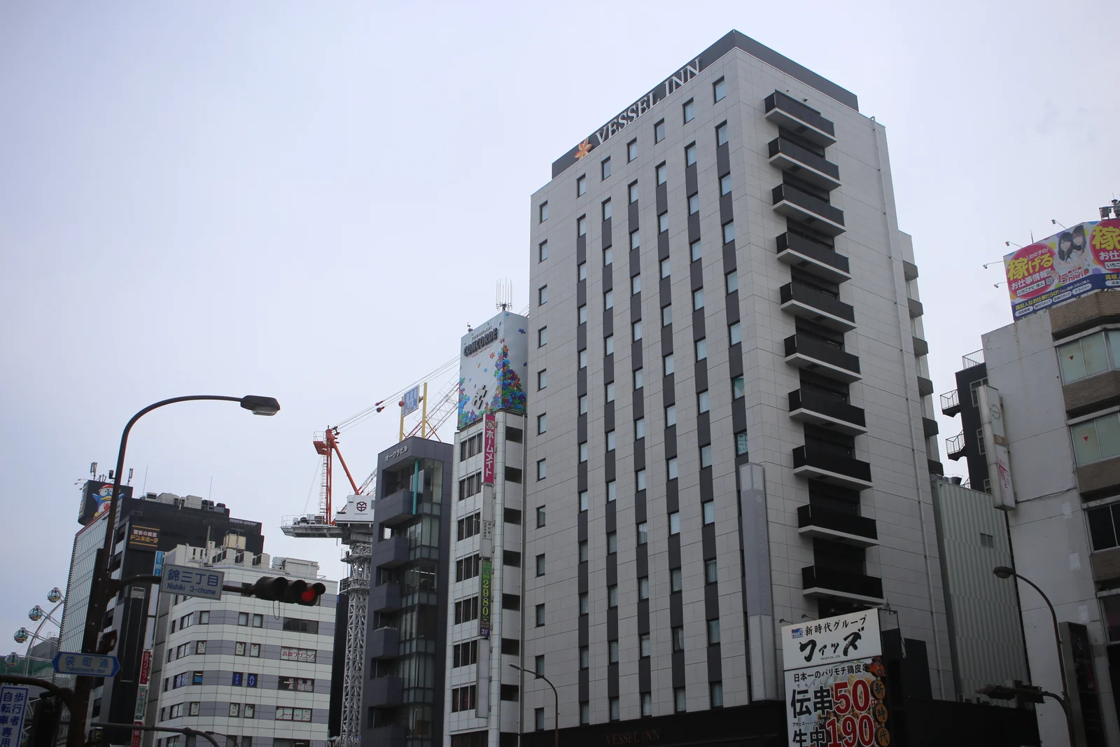꼭대기에 VESSEL INN 간판이 달린 흰색 호텔 건물과 주변 빌딩, 공사 크레인